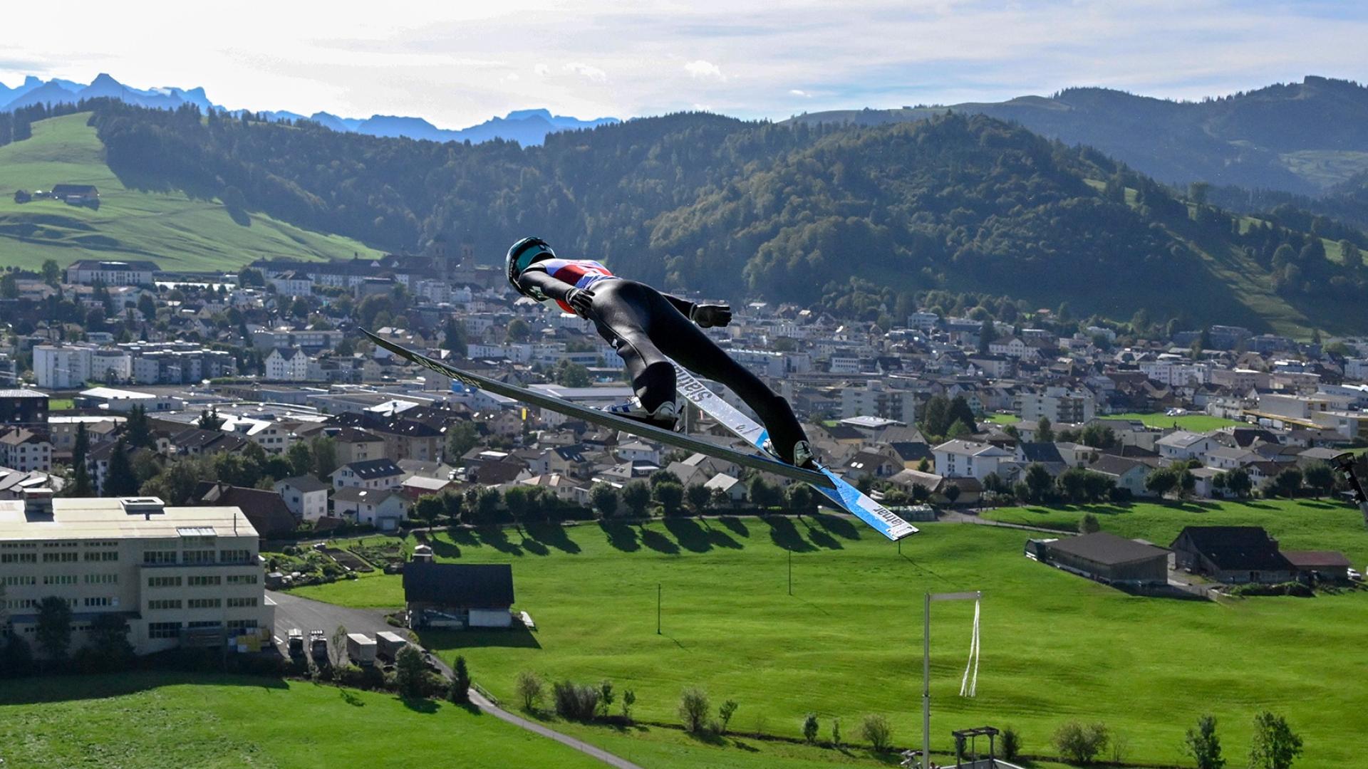 Skispringer mit Dorf im Hintergrund