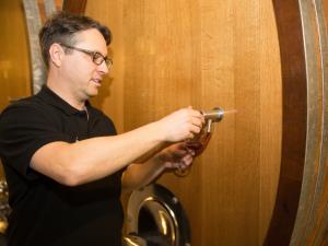 Ein Mann zapft im Weinkeller an einem grossen Fass Wein ab.